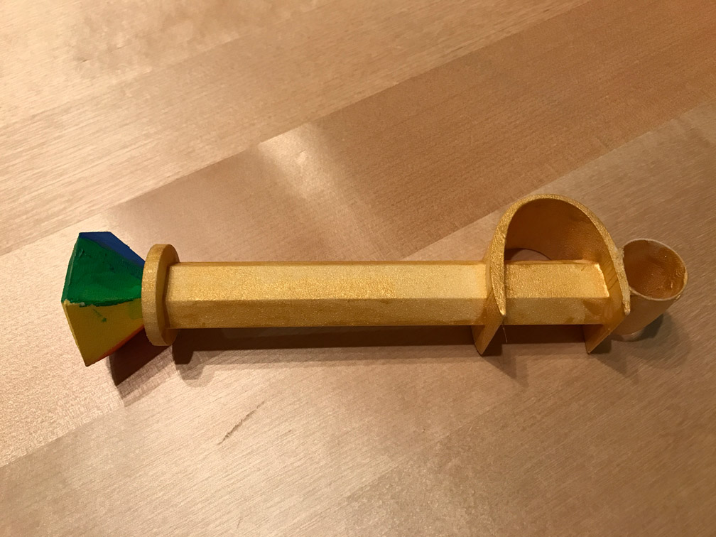 Vue d'un côté de la baguette, avec des facettes verte et jaune du bijou, et baguette dorée