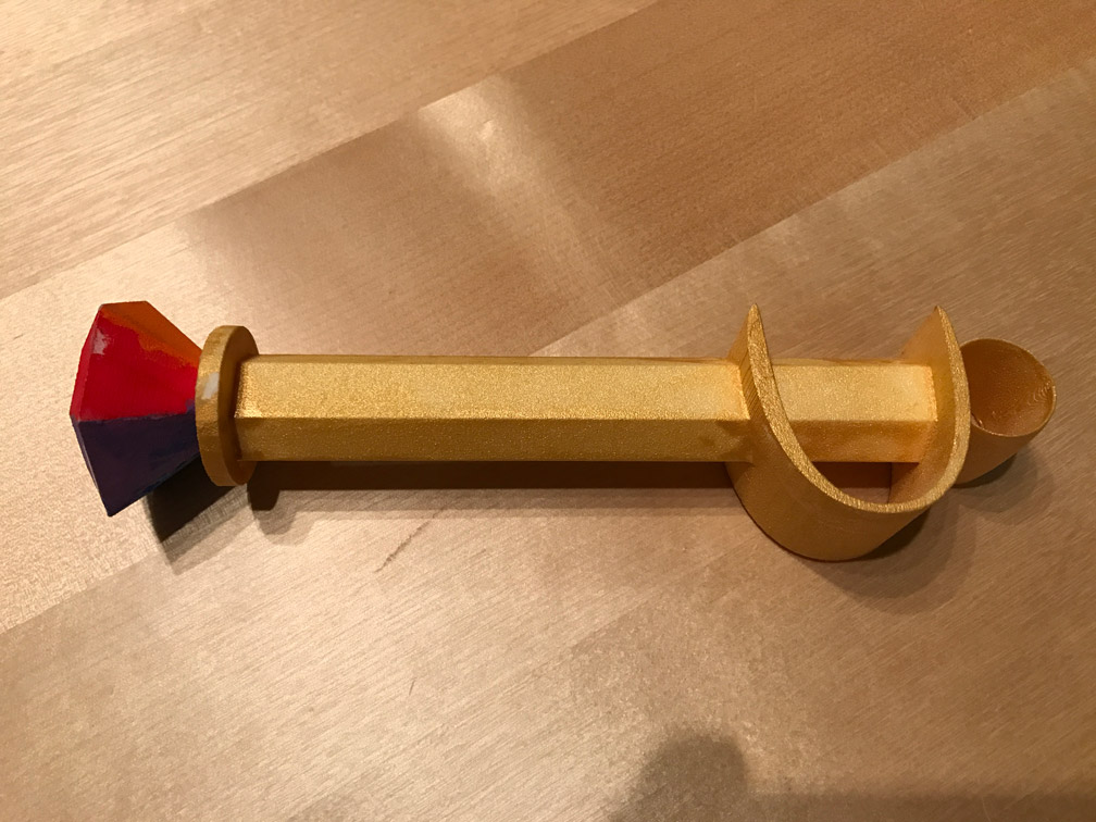 Vue d'un côté de la baguette, avec des facettes rouge et bleue du bijou, et baguette dorée