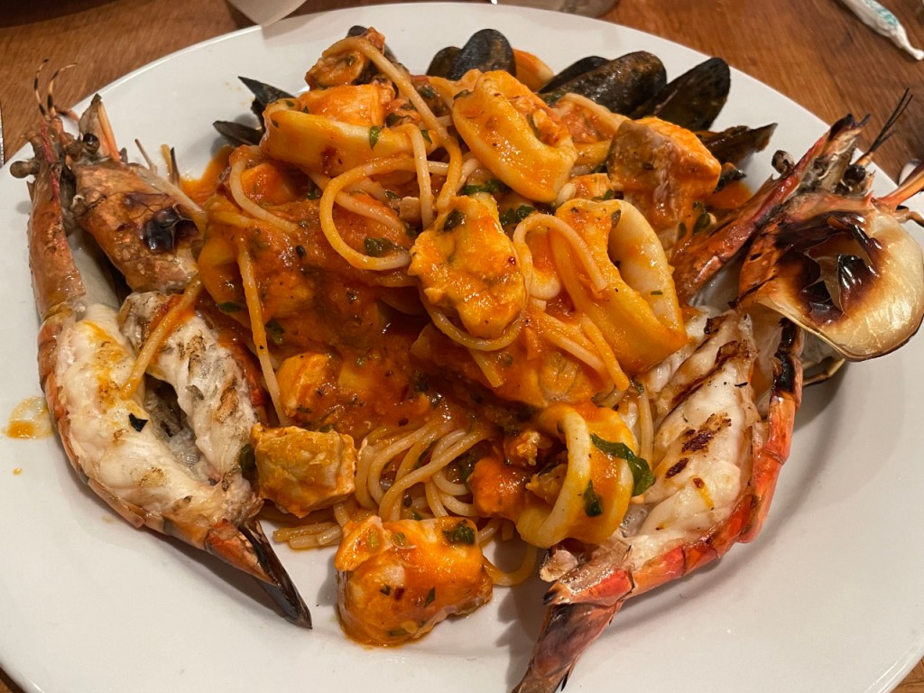 Spaghetti aux fruits de mer -- il y a six moules, des anneaux de calamars, des morceaux d'un poisson inconnu, et une langoustine fendue en deux, tout en haut des spaghettis.