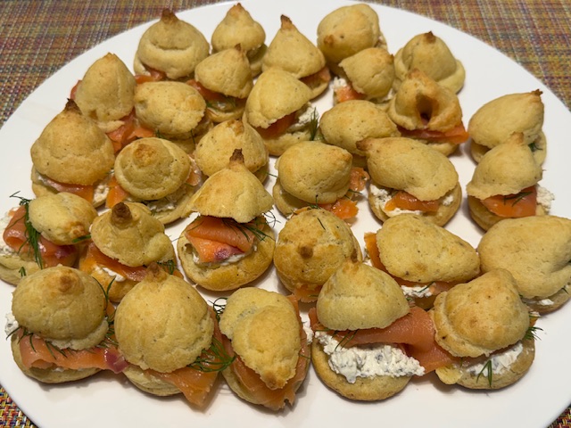 Assiette avec 30 gougères coupées en deux et fourrées avec du fromage à tartiner Alouette, du saumon fumé et de l'aneth.
