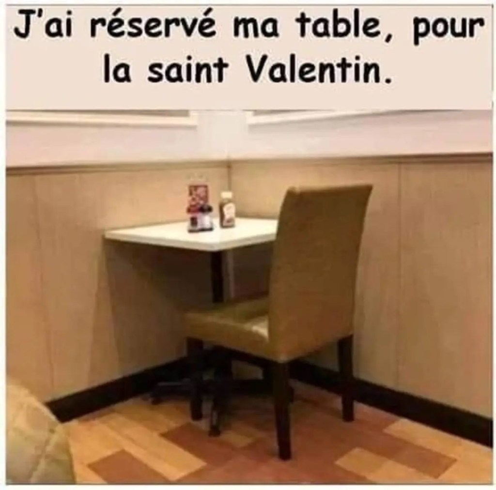 Photo d'une table dans un coin avec une seule place face au mur, et la légende « J'ai réservé ma table pour la Saint-Valentin ».