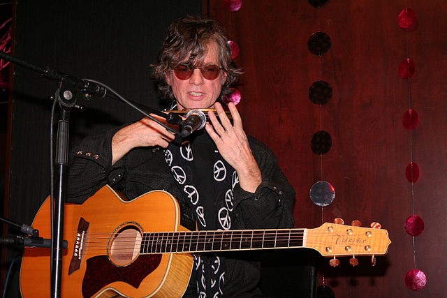 Photo de Paul Personne devant un micro, avec une guitare acoustique