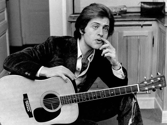Joe Dassin assis avec sa guitare