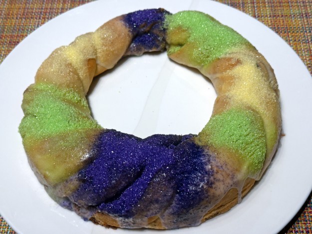 Vue du gâteau "king cake" entier, avec des bandes de sucre coloré en violet, vert et jaune