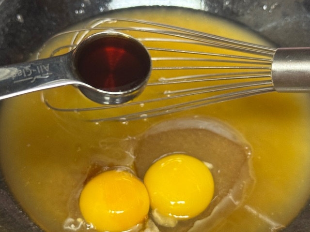 Deux jaunes visibles dans le saladier et une cuillère à café de vanille liquide posée au-dessus