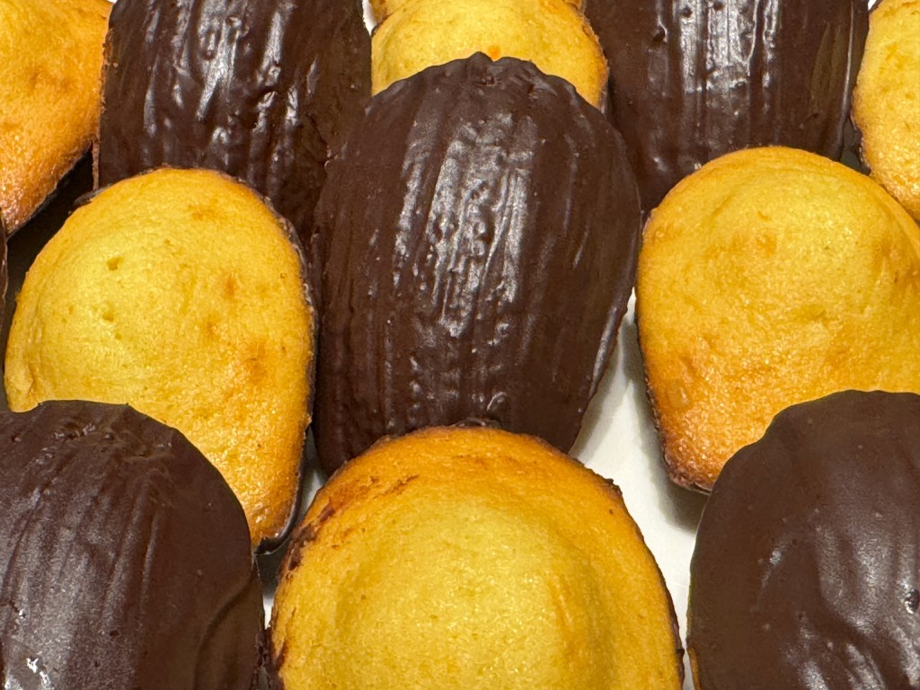 Des madeleines en gros-plan, avec la moitié tournée pour montrer le chocolat, l'autre moitié, la bosse. Il y a des côtés chocolats au centre et aux 4 coins.