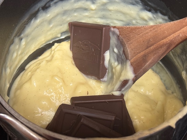 Le reste de la crème à la vanille, toujours dans la casserole, avec des carrés de chocolat noir