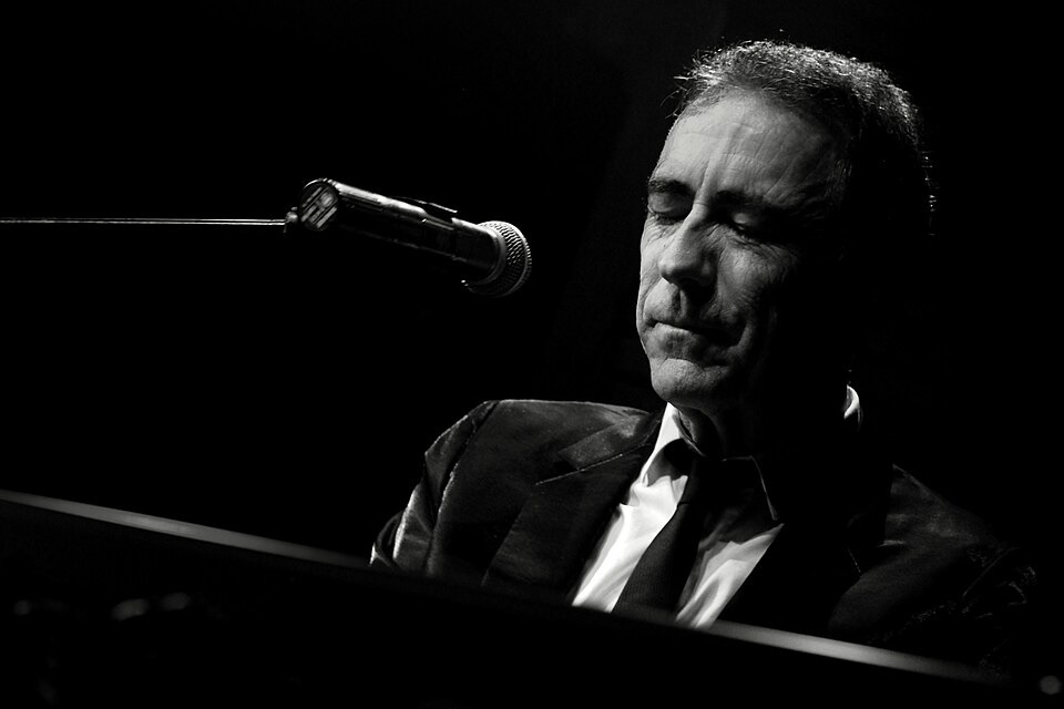 Alain Chamfort assis devant un piano avec un micro en haut