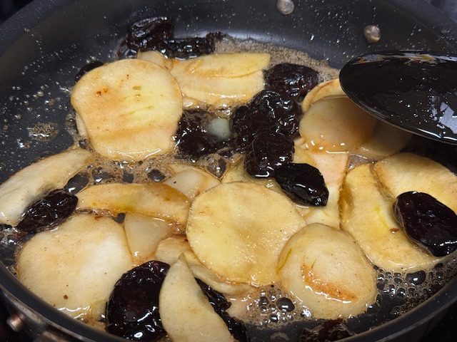 Tranches de pommes, de poires, et de pruneaux en train de se faire caraméliser dans une poêle 