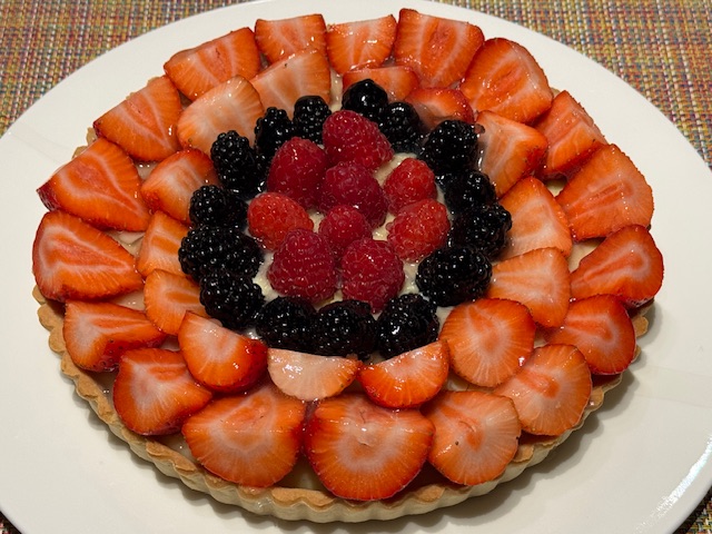 Tarte aux fruits -- il y a deux anneaux de fraises à l'extérieur, suivis d'un anneau de mûres, et à l'intérieur, d'un anneau de framboises. La croûte a été cuite dans un moule flûté.
