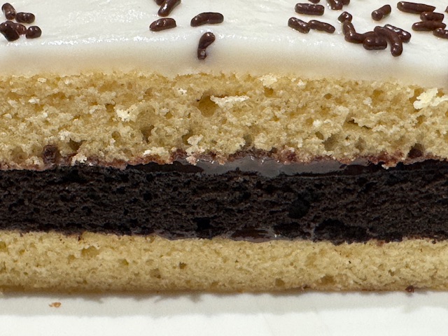 Vue du même gâteau Napolitain, du côté. On voit clairement les trois couches de gâteau -- deux vanille, un chocolat -- les couches de ganache au chocolat, le fondant blanc et les vermicelles au chocolat.