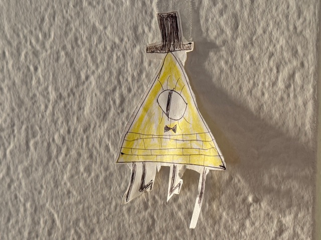 C'est Bill Cipher, dit Bill Crypto en français, dessiné par moi. Il est en forme de pyramide tirée du billet de 1 $ américain, qui a aussi un œil ouvert, un symbole franc-maçon. Où les briques de la pyramide du billet sont verdâtres, Bill est d'un jaune particulièrement vive, à ne pas comme l'or, car pas métallique. Pas comme le billet, il porte un nœud-papillon noir et un haut-de-forme. 