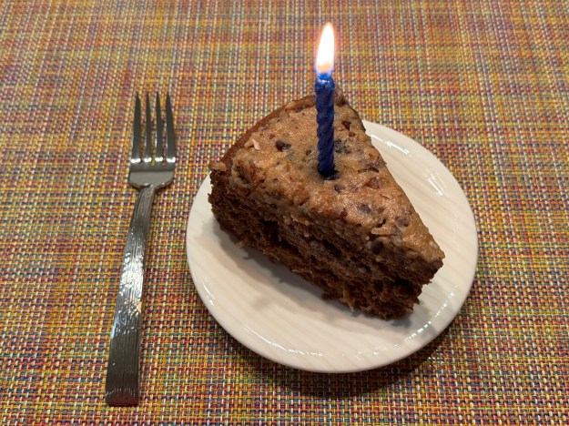 Une part du gâteau. Il y a une chandelle bleue allumée au centre, et une fourchette de dessert à gauche de l'assiette.