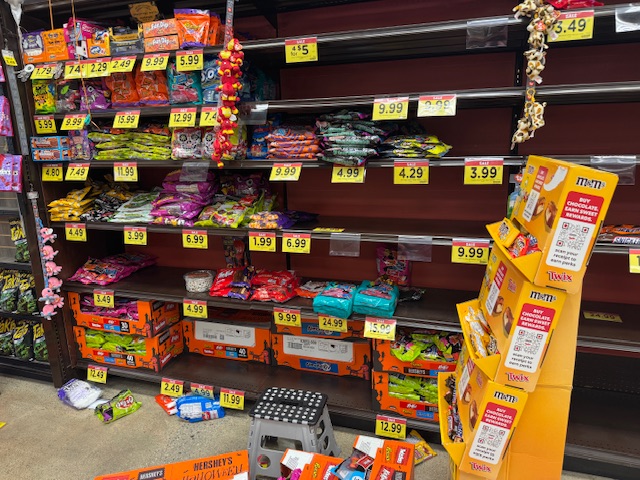 Étagères d'Halloween : le stock qui reste est très mal rangé, et il y a de nombreux sacs de bonbons sur le sol. Pas dans des boîtes, juste éparpillés ici et là.