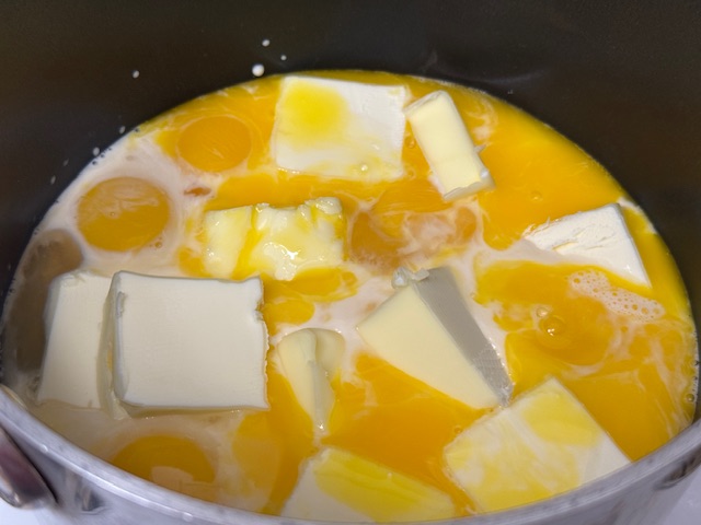 Casserole avec le lait concentré, le beurre, les jaunes et le sucre, au début de la cuisson