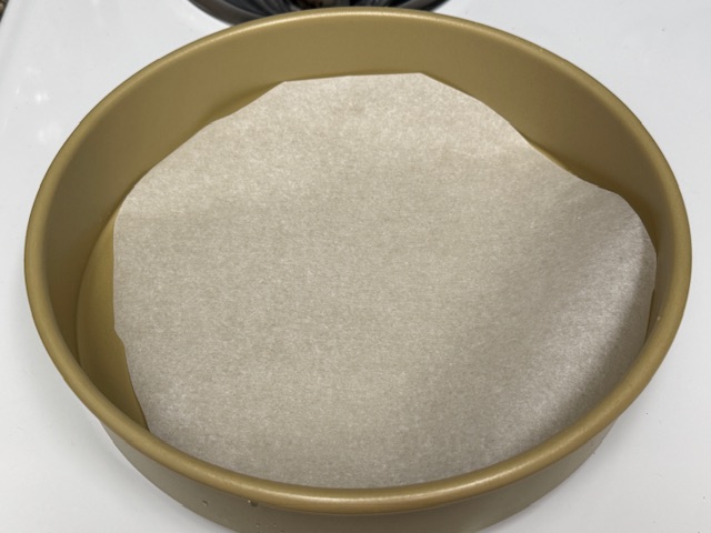 Moule chemisé de papier de cuisson ; le fond est complètement recouvert, mais il y a un petit peu de trop, et le papier atteint les bords.