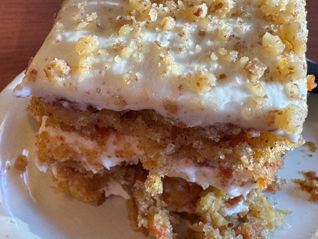 Deux couches de gâteau aux carottes avec deux couches de glaçage au fromage Philadelphia, avec des brisures de noix au-dessus.