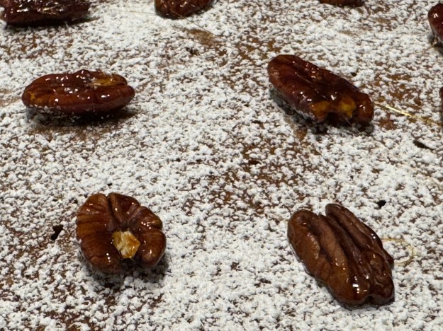 Gros plan des noix de pécan caramelisées sur la surface avec du sucre glace partout. On peut voir tous les cerneaux sont bien enrobés 