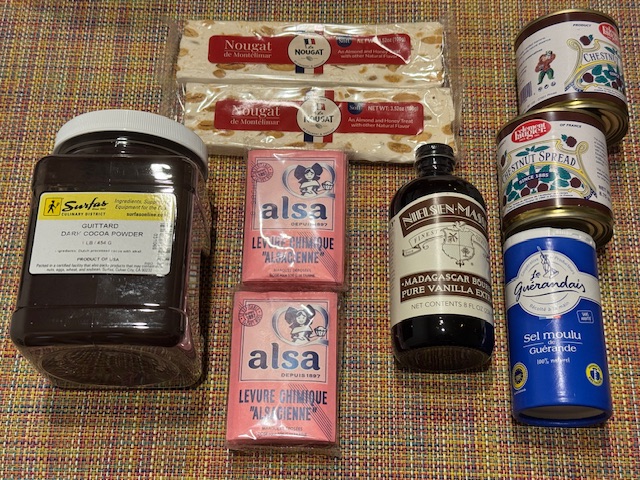 Une boîte de poudre de cacao, deux barres de nougat de Montélimar, une bouteille de vanille liquide, 2 paquets de sachets roses d'Alsa, une boîte de sel guérandais et deux boîtes de crème de marrons