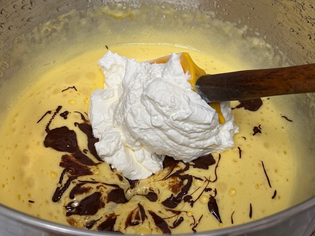 Crème fouettée au-dessus du mélange d'œufs, avec une maryse dans le bol