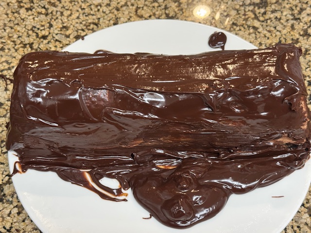 Bûche recouverte de ganache sur une assiette -- il y a de la ganache partout sur l'assiette