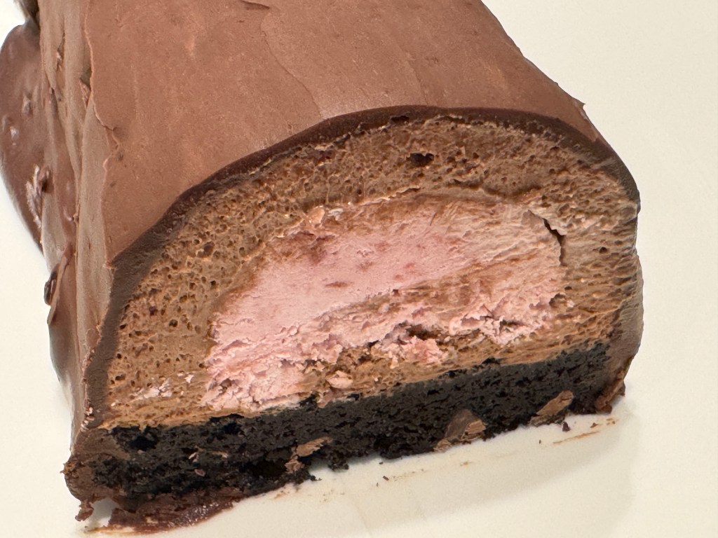 Découpe de la bûche truffe framboise avec son coeur rose, de la mousse au chocolat, un brownie au fond, et recouverte de ganache au chocolat