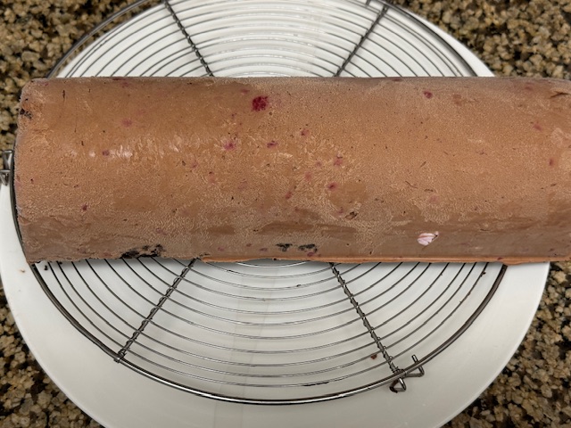 Bûche faite de mousse au chocolat et à la framboise posée sur une grille au-dessus d'une grosse assiette.