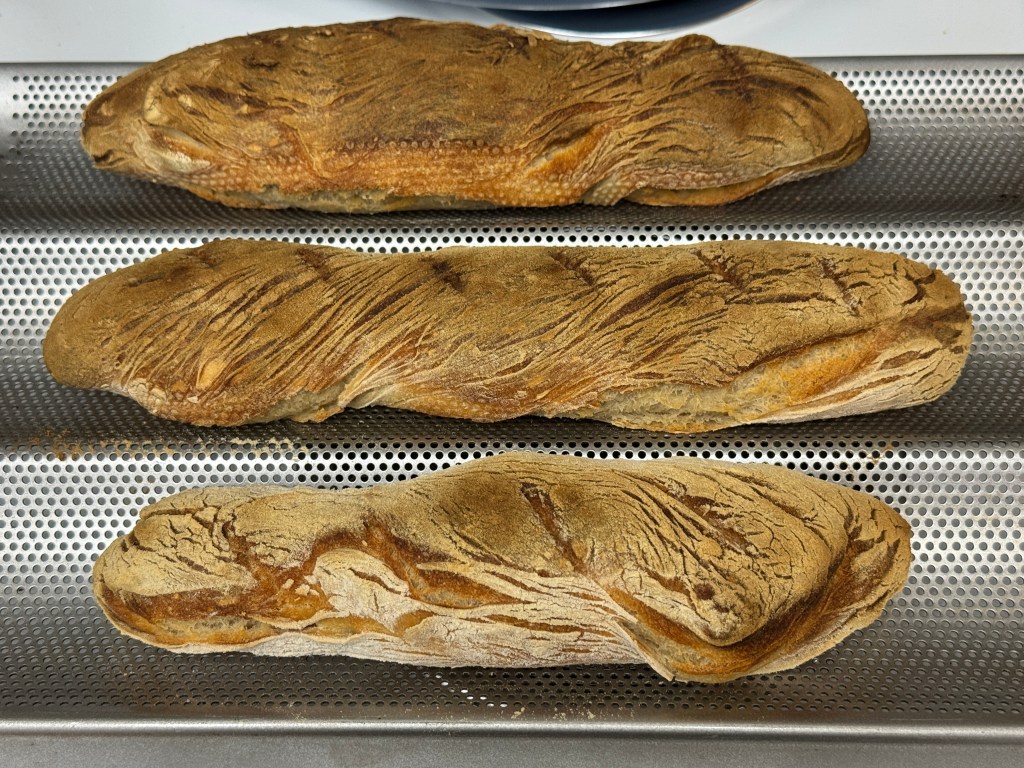 3 baguettes cuites sur un moule à baguette en métal perforé
