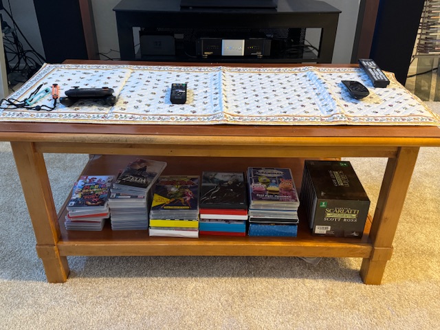 Table basse en bois de cerisier. Il y a un tissu au-dessus, et em bas, des boites pour des jeux vidéo.