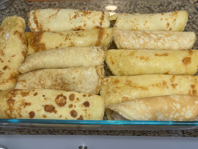 11 crêpes fourrées et roulées dans un plat rectangulaire allant au four
