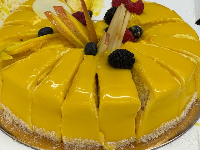 Gâteau à la mangue avec deux couches d'un gâteau à la vanille et trois couches d'un glaçage à la mangue. Il y a quelques fruits rouges au-dessus.