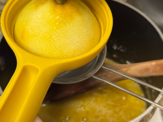 Demi-citron dans un presse-citron posé au-dessus d'un tamis, lui-même posé sur une casserole