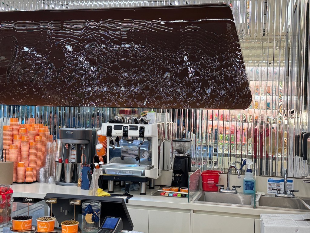 Vue derrière le comptoir --des machines à café, des coupes pour le gelato, mais sur le mur, une cascade de chocolat. 
