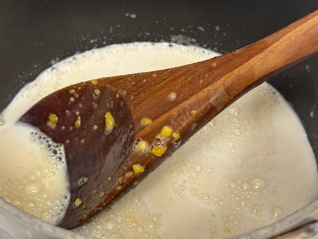 œufs versés dans la casserole. Il y a des grumeaux visibles sur la cuillère en bois
