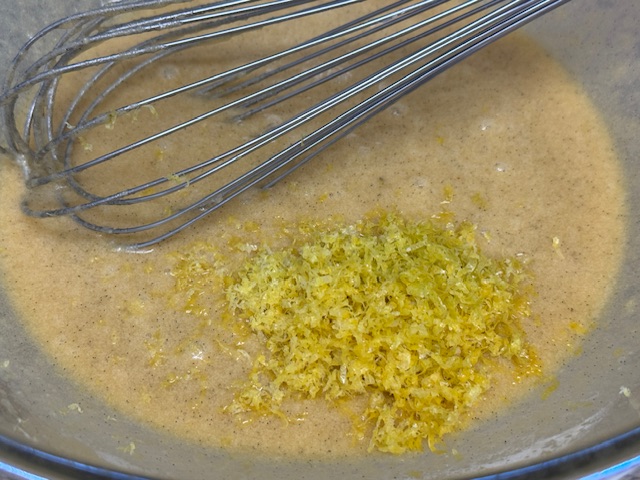 Zeste de citron flottant sur l'appareil autrement fouetté. Le fouet repose sur l'appareil en arrière-plan