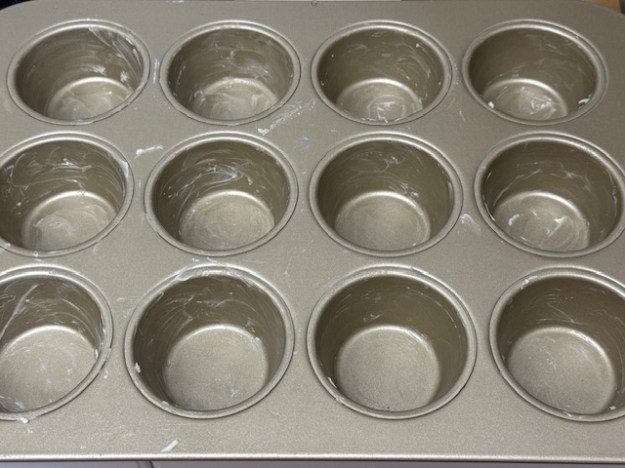 12 puits beurrés d'un moule à muffins en métal.