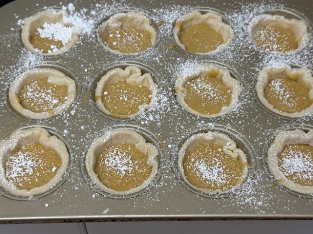Sucre glace tamisé partout au-dessus du moule. Chaque mirliton est bien recouvert, mais la surface du moule aussi.