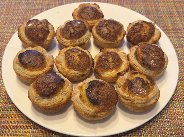 12 mirlitons posés sur une assiette après la cuisson. Ils ont tous de beau feuilletage et des centres gonflés.