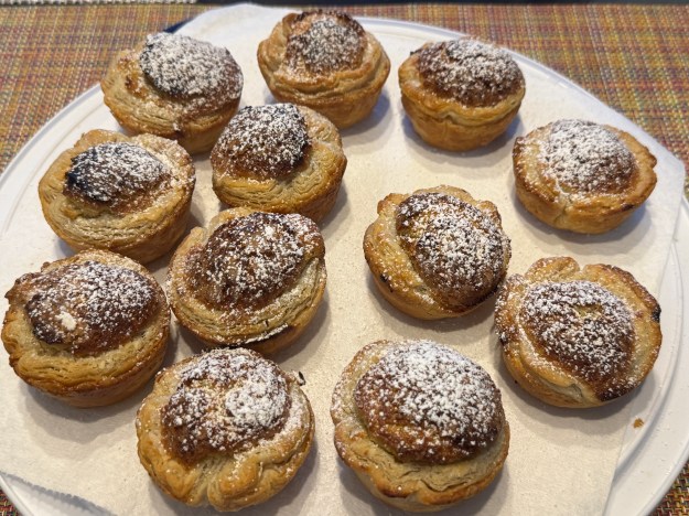 Mirlitons sur une grande assiette en plastique, saupoudrés de sucre glace. Il y a une serviette en papier au-dessous, car