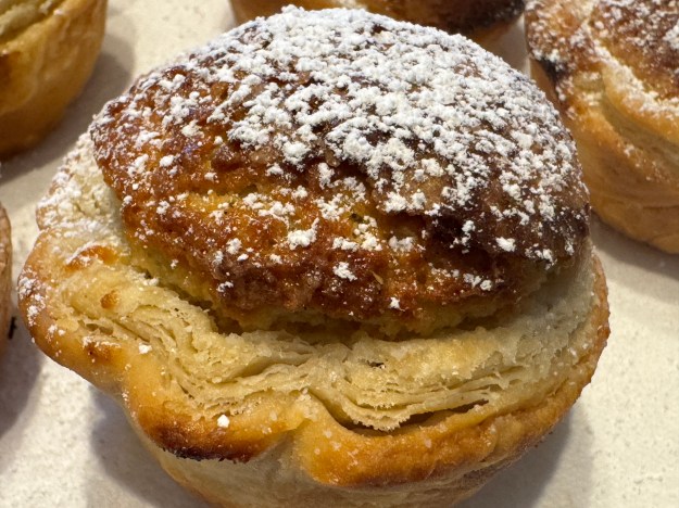 Mirliton en gros-plan ; on peut voir de joli feuilletage tout autour des bords, il y a un centre bien doré et gonflé, et il y a du sucre glace tamisé partout.