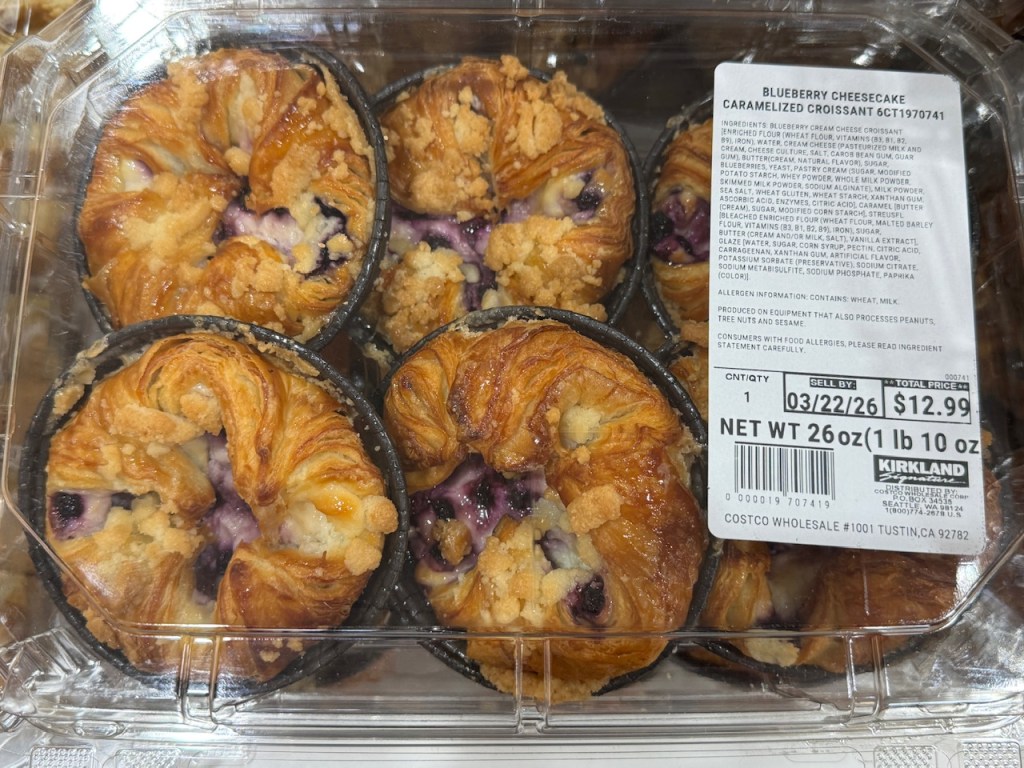 Boîte en plastique avec 6 pâtisseries ronds, presque comme des kouign-amanns individuels, avec les bords pliés vers le centre. Il y a un streusel au-dessus de chacune, et le centre est ouvert -- on peut y voir le soi-disant "cheesecake".