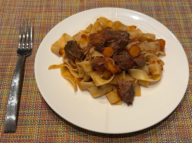 Assiette blanc avec les pâtes au-dessus ; il y a une fourchette à gauche. La viande et des morceaux de carottes sont posées au-dessus des pâtes pour les montrer au monde.