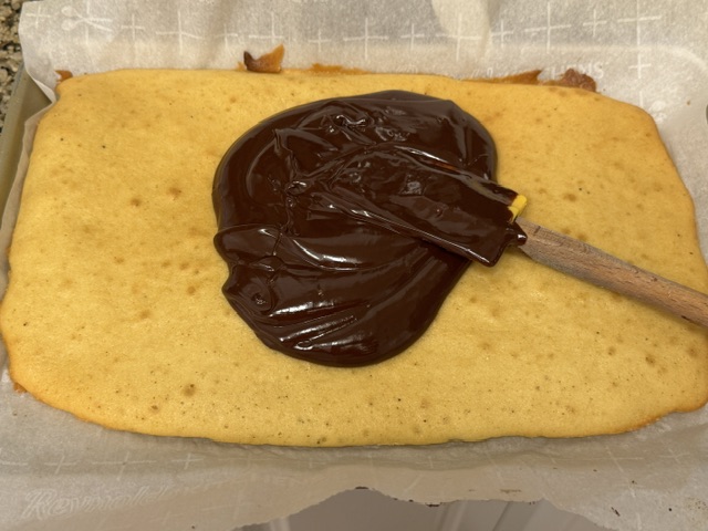 Ganache au chocolat étalée sur la première couche de gâteau à la vanille