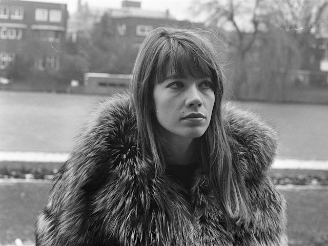 Françoise Hardy à Amsterdam en 1969, au bord d'une rivière. Elle porte un manteau lourd, en fourrure. La photo est en noir et blanc.