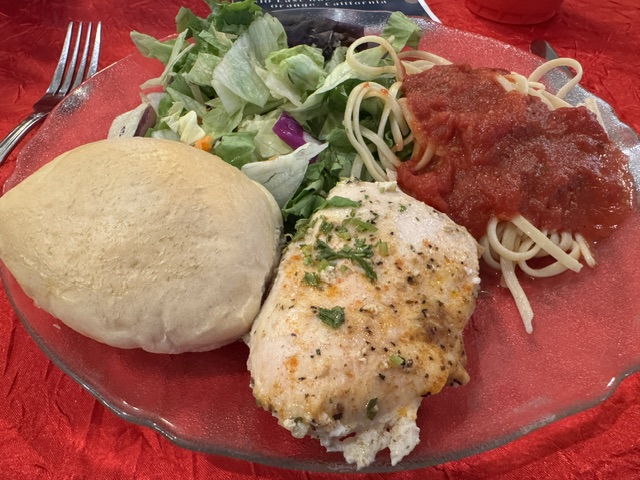 Assiette avec une petite salade verte, un petit pain, un peu de spaghettis et un petite suprême de poulet rôtie.