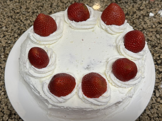 Vue du haut du gâteau -- il y a 8 cercles de chantilly, chacun avec une fraise au centre, autour des bords du haut