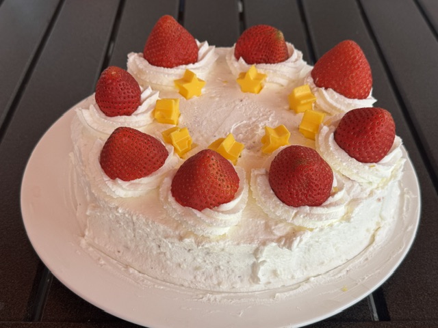 Gâteau entier avec la même chantilly blanche, les mêmes fraises entières et des étoiles jaunes tres similaires.
