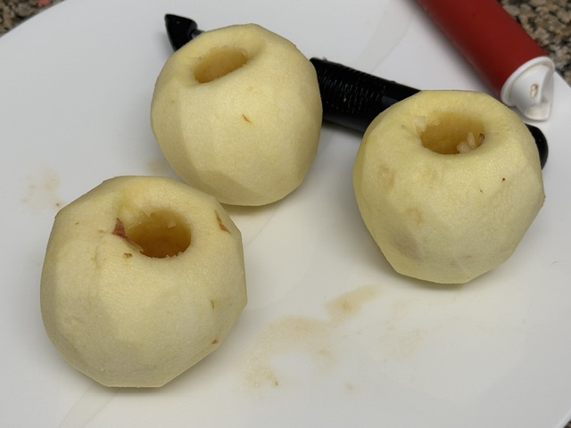 3 pommes vidées et épluchées sur une assiette -- la lame du couteau est visible en haut