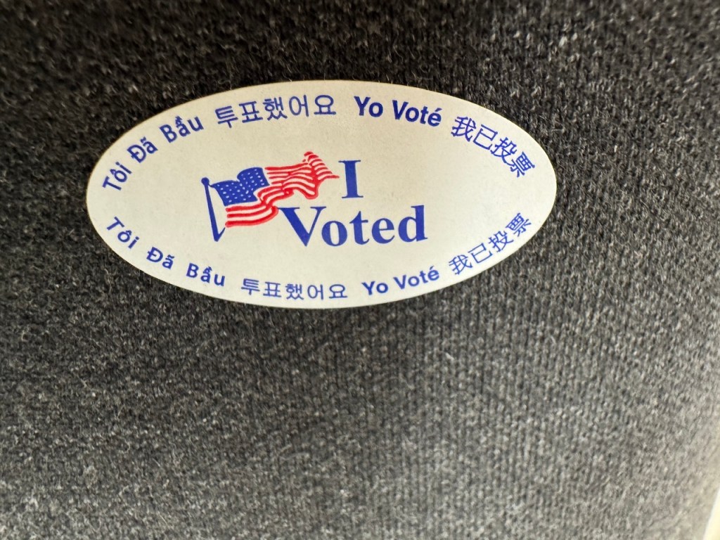 Autocollant blanc avec un petit drapeau américain et les mots "j'ai voté" en anglais, espagnol, coréen, chinois et vietnamien. 