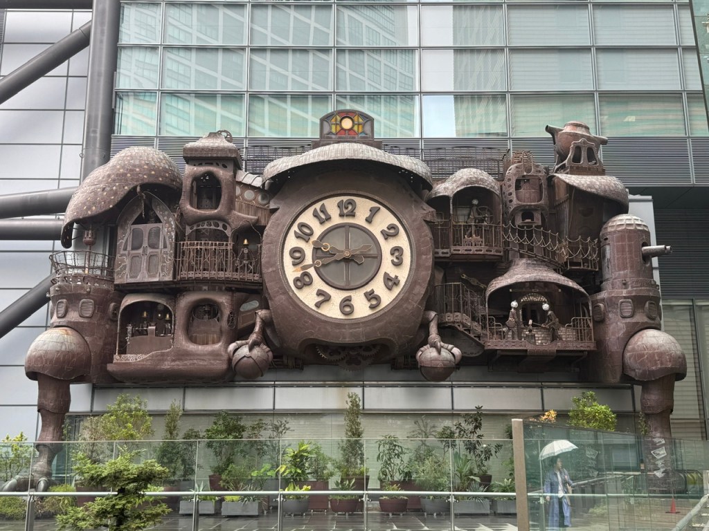 C'est une grosse horloge comme un réveil au centre, mais avec de petits bâtiments aux côtés qui pourraient bien venir d'un film tel que Mon voisin Totoro ou Le voyage de Chihiro.